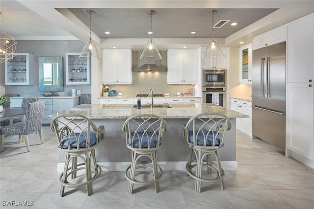 kitchen with built in appliances, white cabinetry, an island with sink, and hanging light fixtures