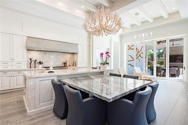 kitchen with light stone countertops, light wood-type flooring, pendant lighting, a center island with sink, and beamed ceiling