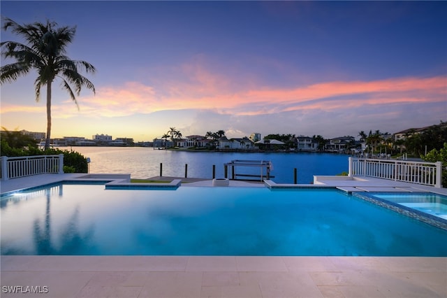 pool at dusk with an in ground hot tub, a water view, and a boat dock