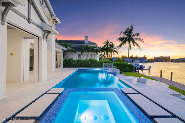 pool at dusk featuring a patio area, an in ground hot tub, and a water view