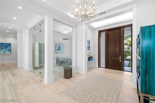 foyer entrance featuring a chandelier, light wood-type flooring, and crown molding