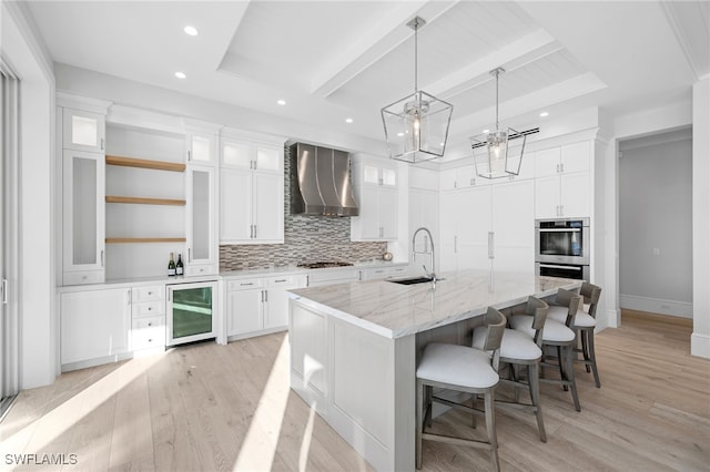 kitchen with white cabinetry, a large island, wall chimney exhaust hood, and beverage cooler