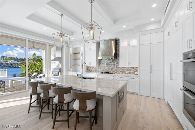 kitchen featuring white cabinetry, sink, wall chimney range hood, light stone counters, and a spacious island