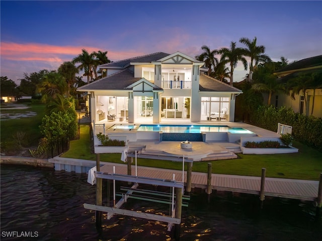 back house at dusk with a patio area, a swimming pool with hot tub, and a balcony