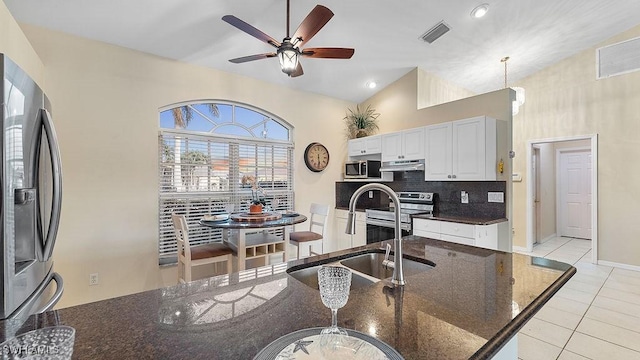 kitchen with dark stone counters, white cabinets, sink, vaulted ceiling, and stainless steel appliances