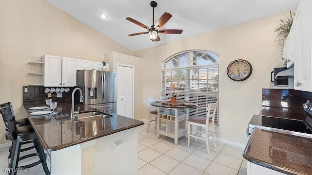 kitchen featuring light tile patterned floors, stainless steel fridge, stove, vaulted ceiling, and white cabinets