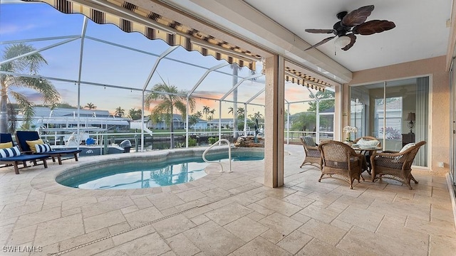 pool at dusk featuring glass enclosure, ceiling fan, and a patio area