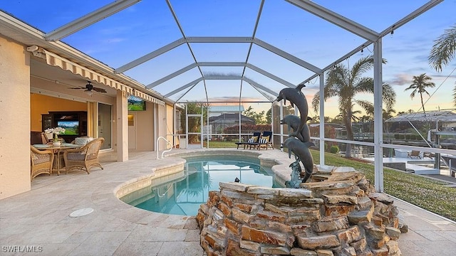 pool at dusk featuring a lanai, a patio area, and ceiling fan