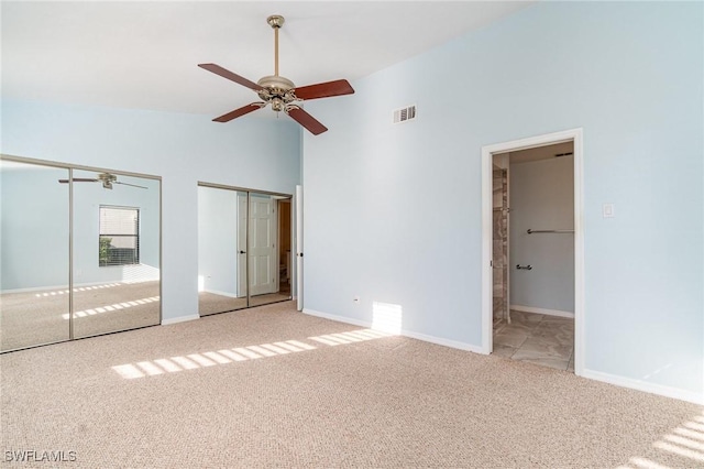 unfurnished bedroom featuring ceiling fan, light colored carpet, high vaulted ceiling, and two closets