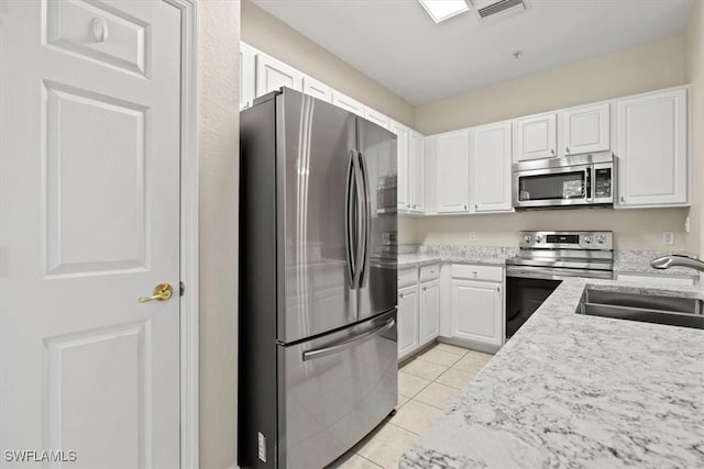 kitchen with sink, light stone counters, light tile patterned floors, appliances with stainless steel finishes, and white cabinets