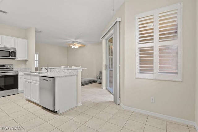 kitchen with light tile patterned flooring, appliances with stainless steel finishes, ceiling fan, a kitchen island with sink, and white cabinets