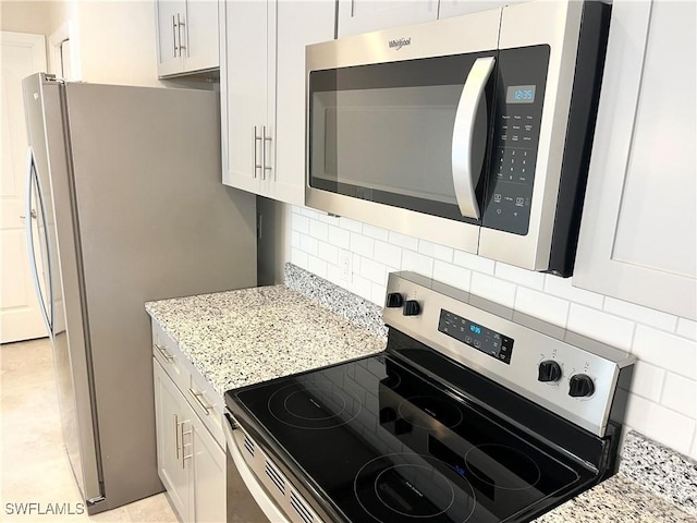 kitchen featuring white cabinets, light stone countertops, stainless steel appliances, and tasteful backsplash