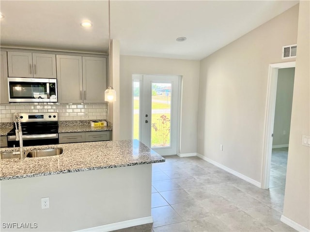 kitchen with backsplash, gray cabinets, light stone counters, and appliances with stainless steel finishes