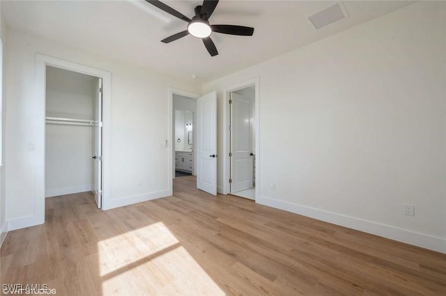 unfurnished bedroom featuring ceiling fan, a closet, a spacious closet, and light hardwood / wood-style flooring