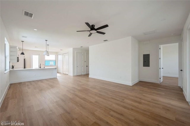 unfurnished living room featuring ceiling fan, sink, electric panel, and light hardwood / wood-style flooring