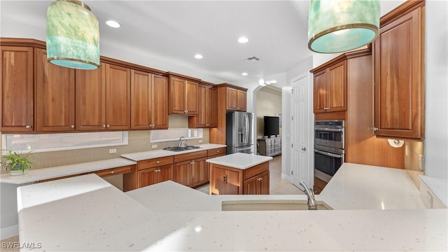 kitchen featuring kitchen peninsula, appliances with stainless steel finishes, light stone counters, sink, and hanging light fixtures