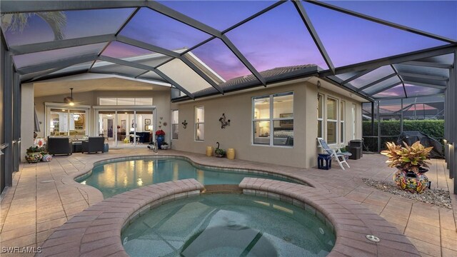 pool at dusk featuring a lanai, an in ground hot tub, a patio, and an outdoor hangout area