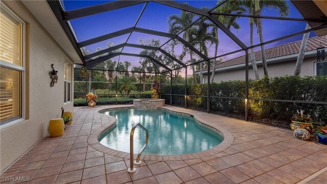 pool at dusk with glass enclosure, an in ground hot tub, and a patio