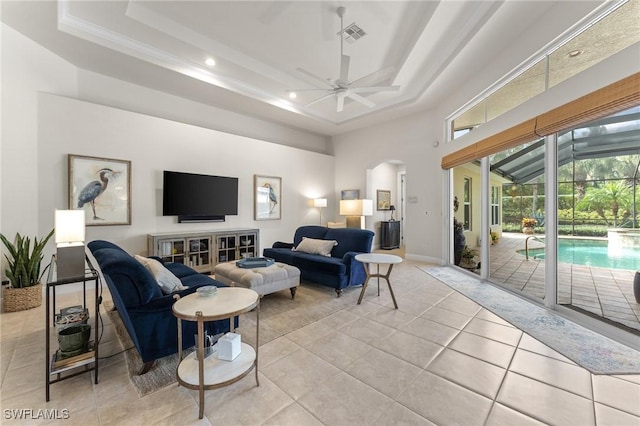 living room with ceiling fan, a raised ceiling, light tile patterned floors, and a high ceiling