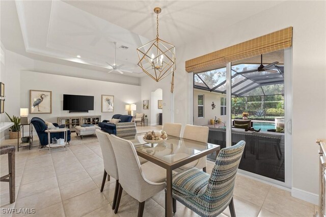 dining space with a raised ceiling, lofted ceiling, light tile patterned flooring, and ceiling fan with notable chandelier