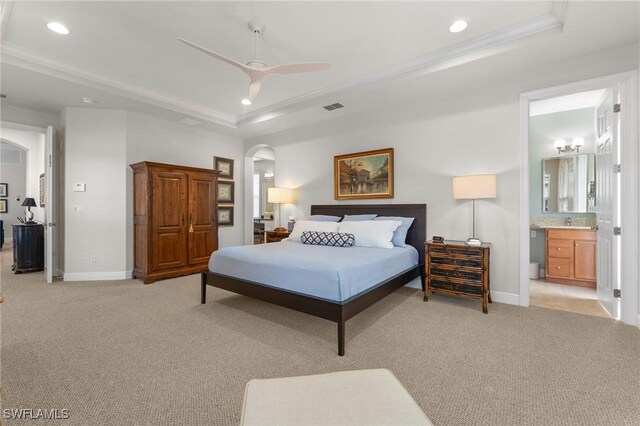 bedroom with a raised ceiling, ensuite bath, ceiling fan, and light carpet