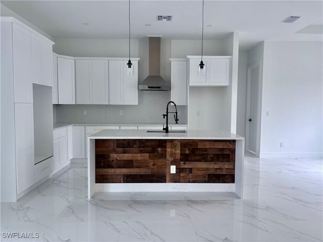 kitchen with white cabinets, pendant lighting, wall chimney exhaust hood, and an island with sink