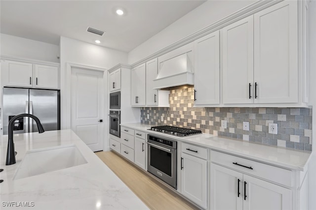 kitchen with white cabinets, sink, premium range hood, and appliances with stainless steel finishes