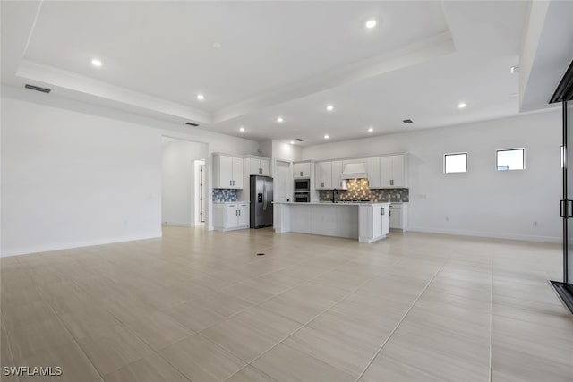 unfurnished living room featuring a tray ceiling, sink, and light tile patterned floors