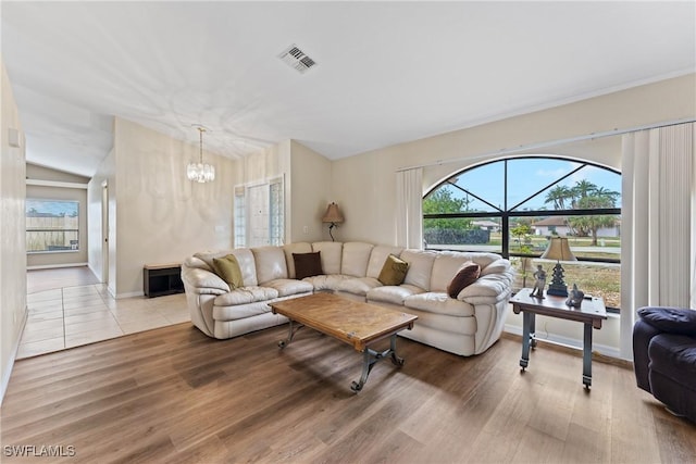 living room with hardwood / wood-style floors, a notable chandelier, and vaulted ceiling