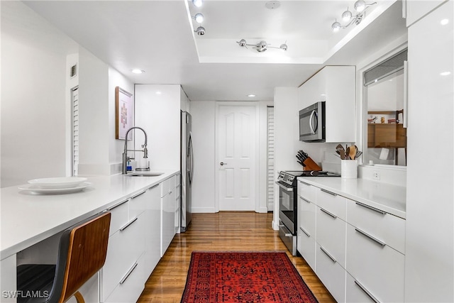 kitchen with hardwood / wood-style floors, sink, white cabinets, and stainless steel appliances