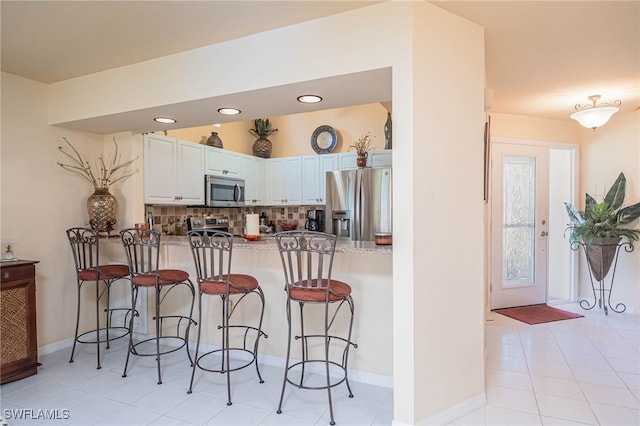 kitchen featuring decorative backsplash, stainless steel appliances, white cabinetry, and a breakfast bar area