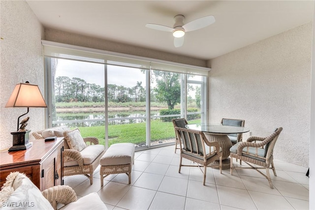 sunroom with ceiling fan and a water view