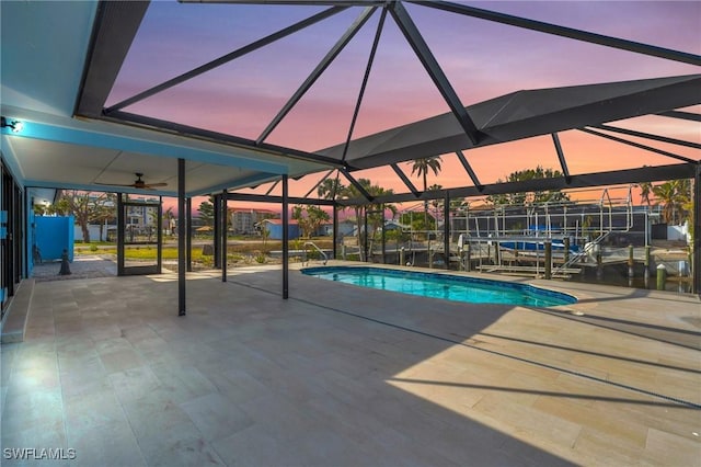 pool at dusk featuring glass enclosure and a patio