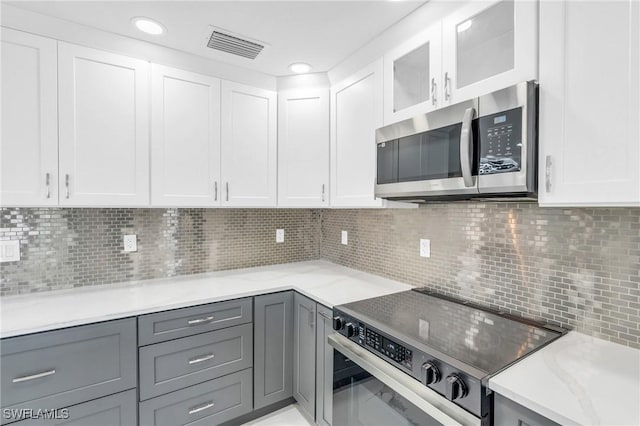 kitchen with decorative backsplash, appliances with stainless steel finishes, white cabinetry, and gray cabinetry