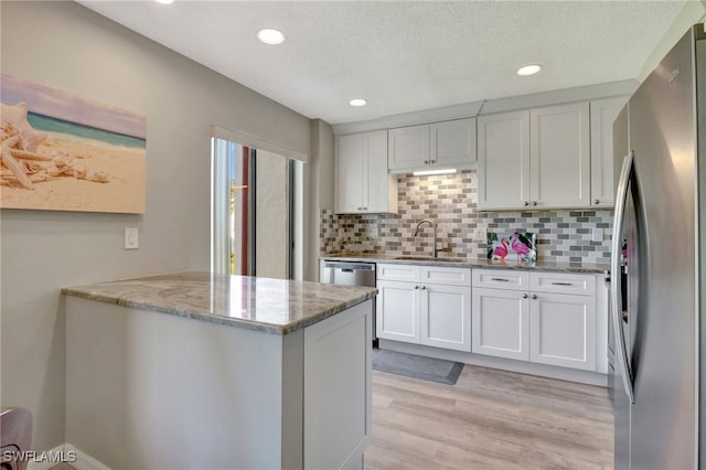 kitchen with light wood finished floors, stainless steel appliances, white cabinetry, a sink, and light stone countertops