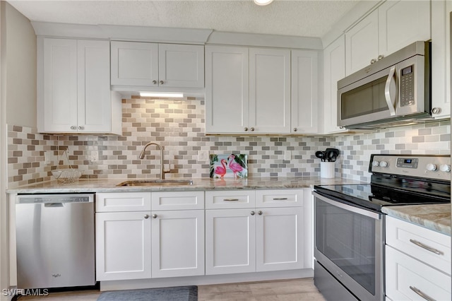 kitchen with appliances with stainless steel finishes, a sink, light stone counters, and white cabinets