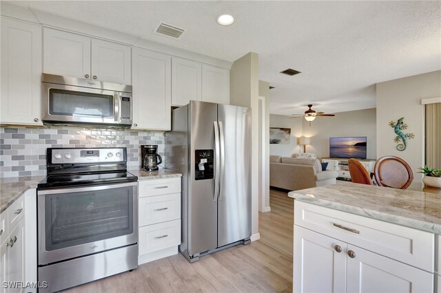 kitchen with light stone counters, light wood-style flooring, stainless steel appliances, visible vents, and white cabinets