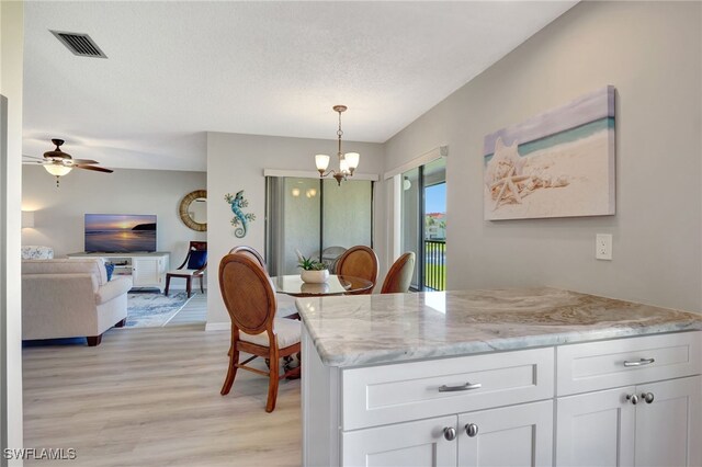 kitchen featuring pendant lighting, visible vents, white cabinets, light stone countertops, and light wood-type flooring