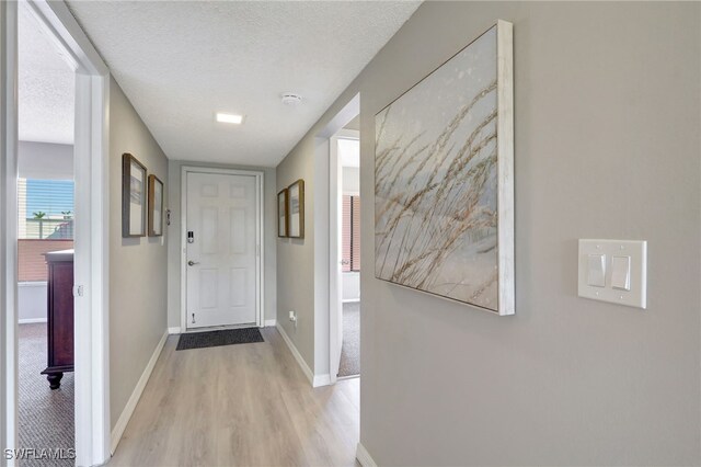 doorway featuring light wood-style flooring, a textured ceiling, and baseboards