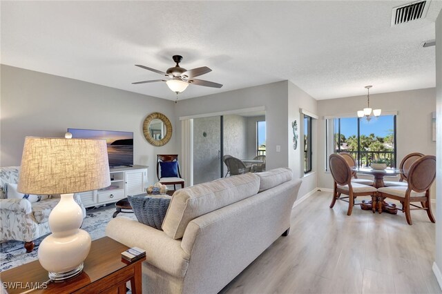 living area with light wood-type flooring, visible vents, a textured ceiling, and ceiling fan with notable chandelier