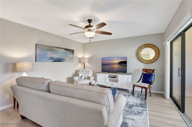 living room featuring light wood-style flooring, a textured ceiling, baseboards, and a ceiling fan