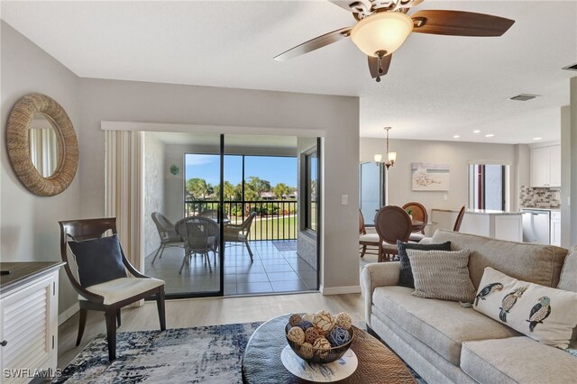 living room with baseboards, ceiling fan with notable chandelier, visible vents, and light wood-style floors