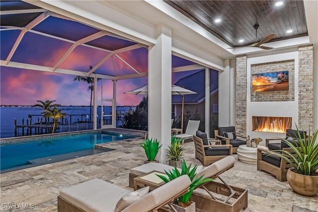 pool at dusk featuring a water view and a brick fireplace