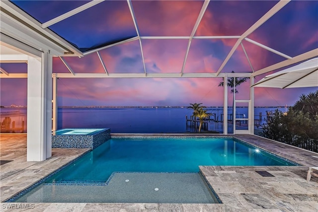 pool at dusk featuring an in ground hot tub, a water view, and a patio