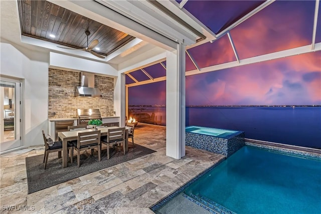 patio terrace at dusk with a water view, area for grilling, a grill, and a pool with hot tub