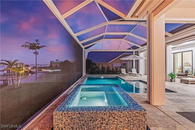 pool at dusk featuring a lanai, a patio, and an in ground hot tub