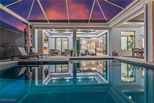 pool at dusk with an outdoor hangout area, a patio, and glass enclosure