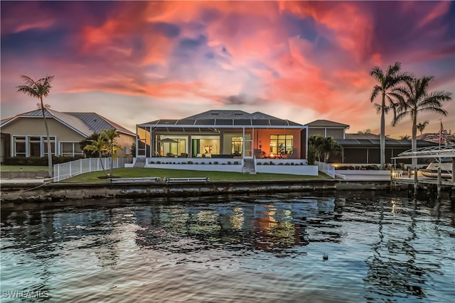 back house at dusk with a water view, a lanai, and a yard