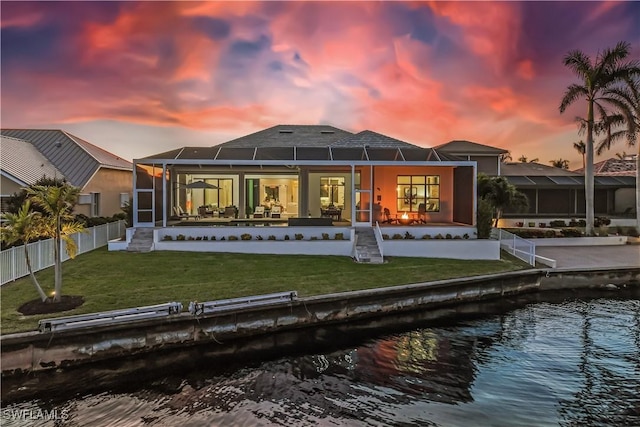 back house at dusk featuring a lanai, a lawn, a patio, and a water view