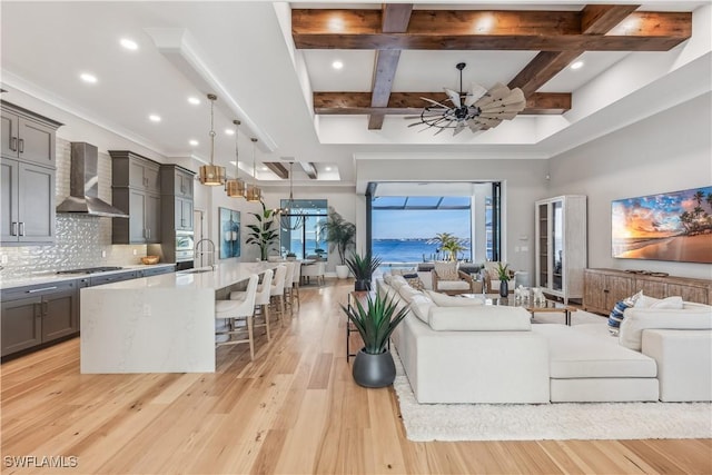 living room with ceiling fan, sink, beam ceiling, and light hardwood / wood-style flooring